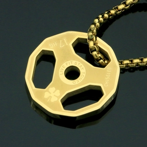Macro shot of gold dumbbell weight plate pendant with motivational fitness engraving