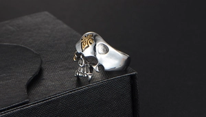 Detailweergave van zilveren punk schedelring met gouden schoppen embleem en vintage finish