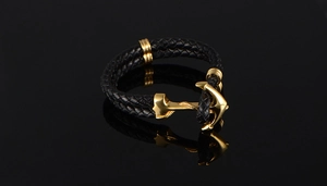 Macro di bracciale da uomo in pelle nera intrecciata con chiusura ad ancora dorata e riflesso nitido