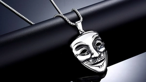 Macro view of polished V for Vendetta mask pendant on a bead chain over black leather