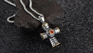 Macro view of bicolor cross pendant with red gemstone and textured engraving