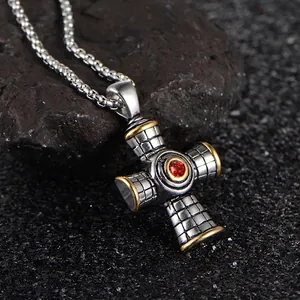 Silver and gold cross necklace with red gemstone on black volcanic rock background