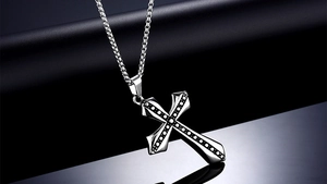 Macro shot of silver stainless steel cross pendant with textured dots on a box chain link