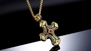 Macro view of gold stainless steel cross pendant with red zircon and embossed patterns