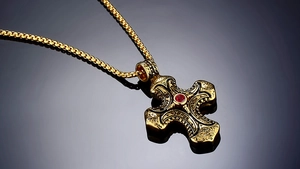 Macro view of ornate gold cross pendant with red zircon and vintage engraving details