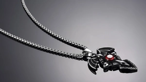 Macro detail of gothic cross necklace with bat wings and a red gemstone on dark metal