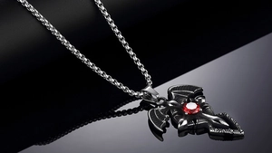 Macro shot of gothic cross necklace with bat wings and red faceted gemstone