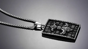 Macro shot of punk shield pendant with fleur-de-lis motif and steel box chain