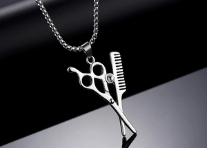 Détail du pendentif ciseaux et peigne en acier avec chaîne sur fond noir poli