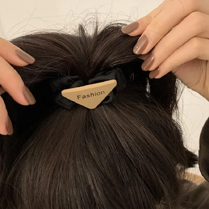 Minimalist black fabric scrunchie with triangle logo plaque on elegant ponytail