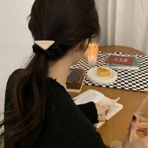 Minimalist black scrunchie with triangle charm worn in a ponytail by female model