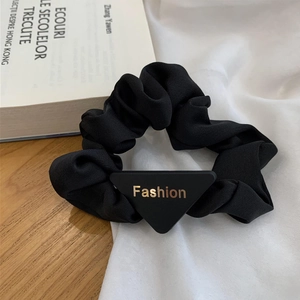 Detailed macro shot of a black fabric hair scrunchie with a gold Fashion triangle plate