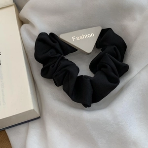 Detailed shot of black scrunchie with triangular Fashion tag on a white fabric background