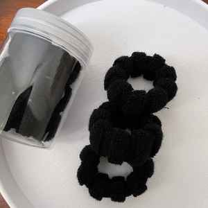 Detailed view of high-elastic black hair ties in a clear storage jar on a white tray