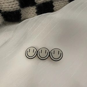 Détail macro de trois smileys gris sur une pince à cheveux en métal doré chic