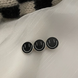 Détail d'une pince à cheveux avec trois badges sourire noirs sur un tissu blanc doux