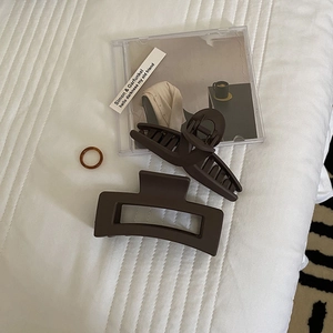 Minimalist matte brown hair clips and amber ring displayed on soft white fabric background