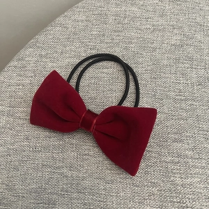 Détail d'un chouchou en velours rouge foncé avec doubles élastiques noirs sur tissu gris