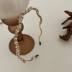 Elegante Franse gouden golf hoofdband met witte parels op een keramische houder