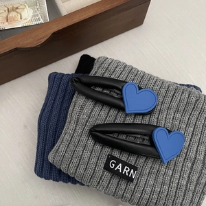 Vintage black leather hair clips with blue heart charms on gray knitted fabric background
