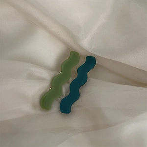 Détail de barrettes à cheveux ondulées en acétate vert et bleu sur tissu de soie