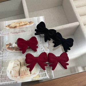 Close-up of elegant red and black velvet bow hair clips with pearls on a white tray