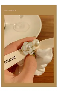 Detail of a white silk scrunchie featuring camellia charm, pearls, and a branded ribbon