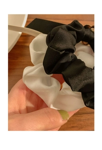 Detail of black and white satin scrunchies with metallic accents on a wooden background