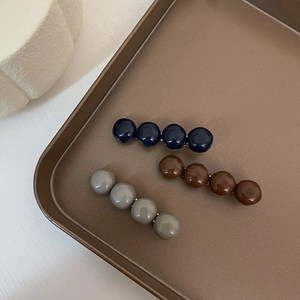 Three minimalist colorful resin ball hair clips displayed on a brown metal tray