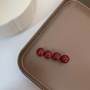 Detail view of burgundy glossy bead hair clip on a vintage dark metallic tray