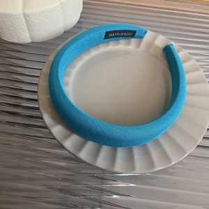 Detail of bright blue twill fabric headband with handmade label on white ceramic plate
