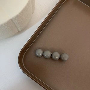 Close-up of four glossy grey beads on a minimalist metallic hair clip in a tray