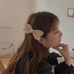 Elegant beige bow hair clip with pearl embellishment worn by a model in warm light