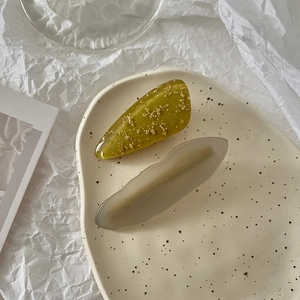 Detail of amber and green resin hair clips with gold foil on a ceramic tray
