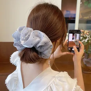 Détail d'un grand chouchou à pois en tissu de soie bleu gris clair sur un chignon flou