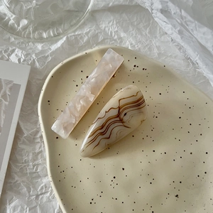 Detail of pink marble and amber textured hair clips on an artistic beige tray