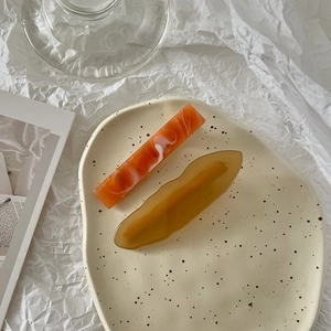 Detailed macro of orange marble and amber yellow wave acrylic hair clips on a tray