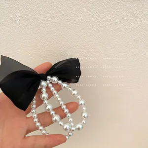 Detail of elegant black mesh bow hair tie with triple-layered gradient pearl strands