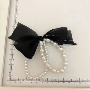 Detail of double-layered black mesh bow with white pearls on a flexible hair tie bracelet