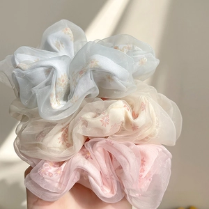 Close-up of three organza mesh scrunchies with delicate floral prints in blue white and pink