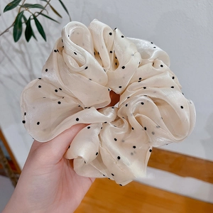 Détail d'un grand chouchou crème à pois noirs en tissu soyeux et translucide élégant