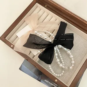 Detail of double-layer pearl hair tie with oversized champagne and black organza bows