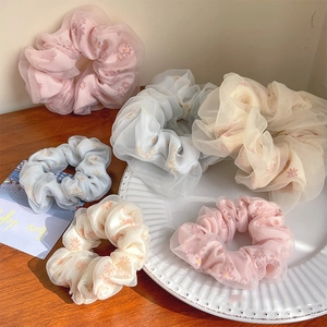 Detail view of double-layered mesh hair scrunchies with floral patterns on a ceramic tray
