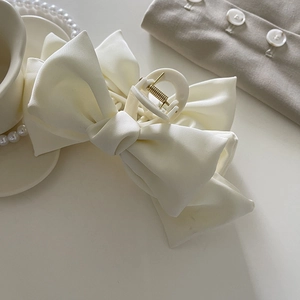 Détail de la pince à cheveux avec nœud en satin blanc montrant la texture du tissu doux