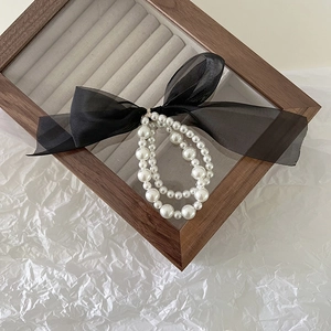 Detail of elegant double-layered pearl hair tie with large black organza bow on wood tray