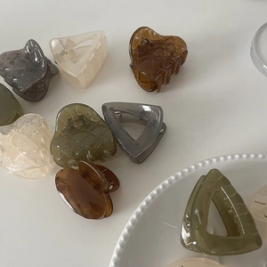 Various acrylic hair claws in heart and triangle shapes with textured amber and olive finishes