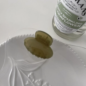 Close-up of small olive green translucent hair claw clip on a white ceramic plate