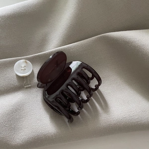 Pince à cheveux élégante en acétate marron foncé pour femme sur fond texturé neutre