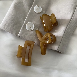 Three amber resin hair clips in various geometric shapes on a stylish beige blazer background