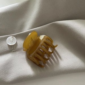 Détail d'une pince à cheveux en acétate ambré sur tissu beige avec une finition brillante